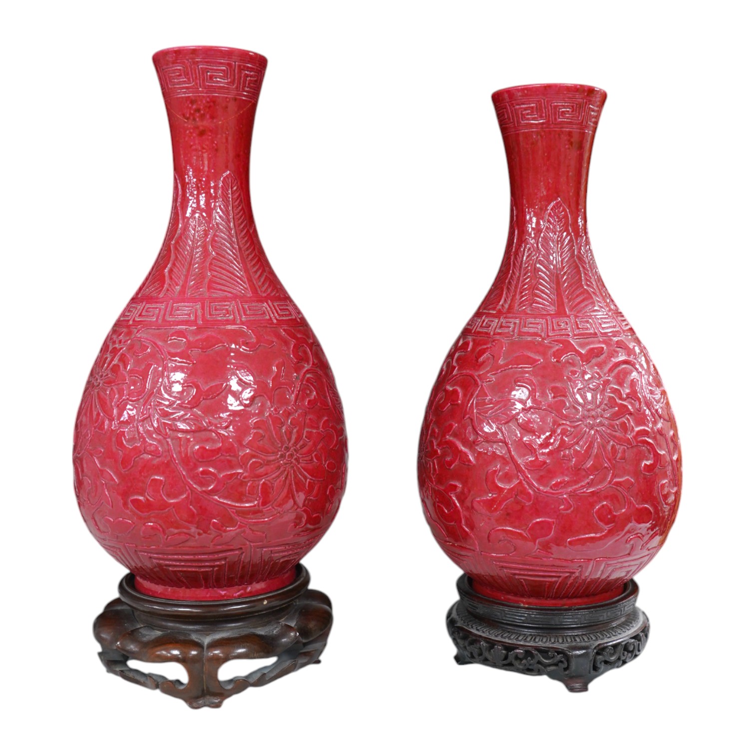 A pair of Chinese ruby ground ‘lotus’ bottle vases, late 19th century, each carved in relief with lotus flowers, scrolling tendrils and leaves, both with carved stands, 24cm high. Condition - one vase the neck broken bot